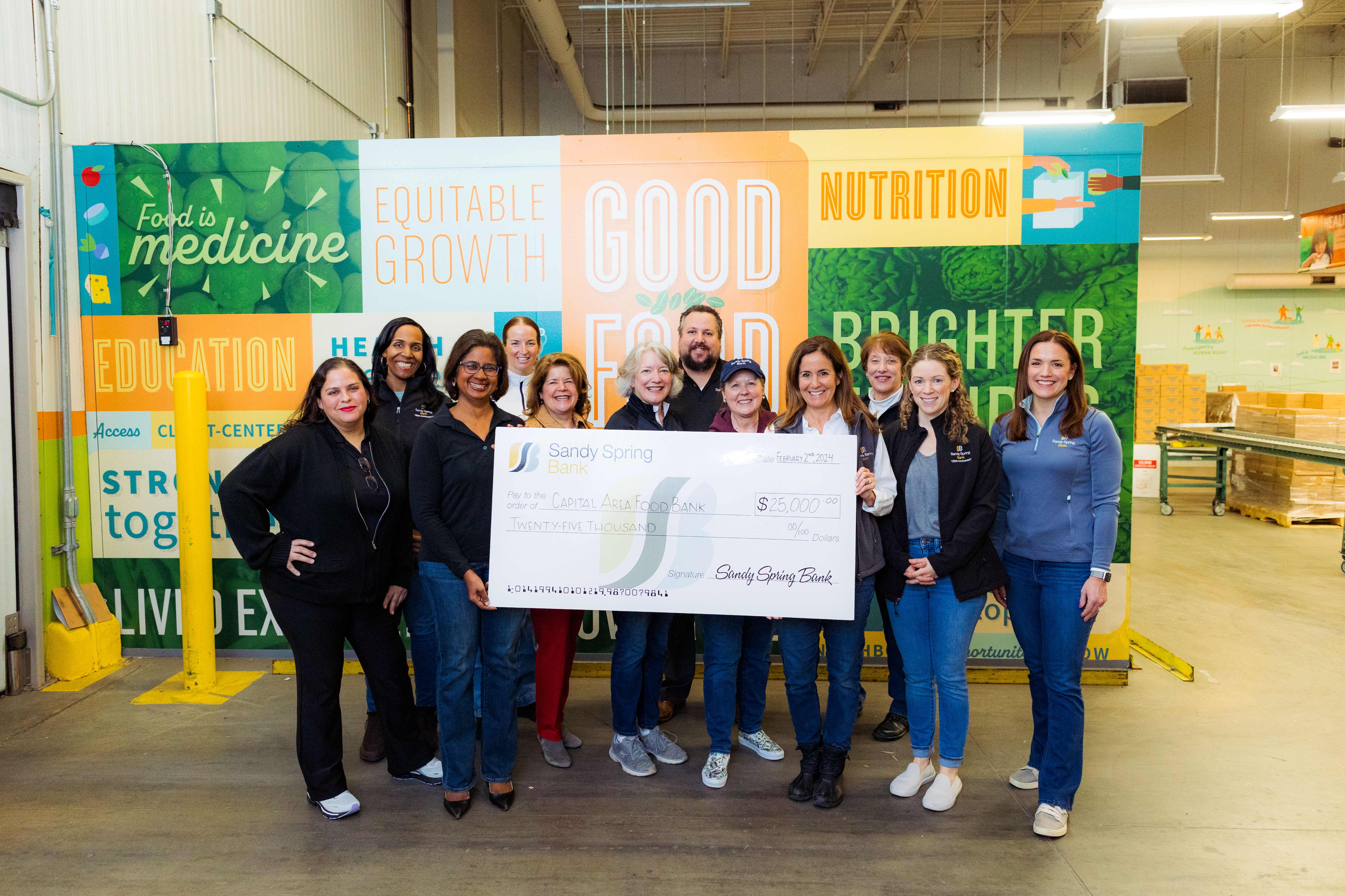 Sandy Spring Bank volunteers at Capital Area Food Bank. Check presentation in front of Capital Area Food Bank signage in the warehouse.